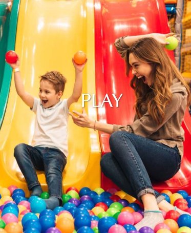 A woman and child joyfully playing together in a colorful ball pit at a kids' play area.