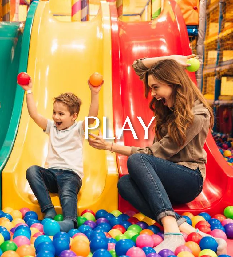 A woman and child joyfully playing together in a colorful ball pit at a kids' play area.